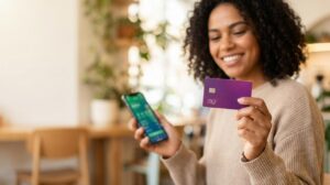 Mulher brasileira segurando um cartão roxo estilo Nubank e um celular com o app de controle de gastos visível em desfoque